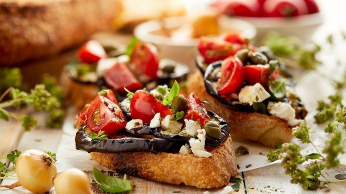 A plate of bruschetta surrounded by fresh herbs, bread and vegetables