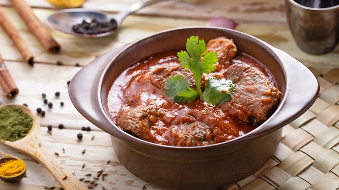 A small bowl of rich lamb rogan josh topped with a green leafy garnish