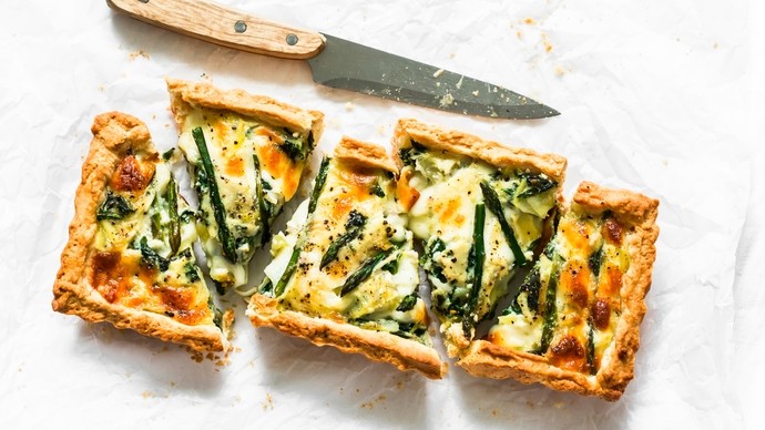 Crusty vegetable pie cut into slices layered with cheese and green veggies