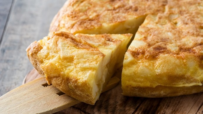 A wooden serving spatula picking up a section of Spanish omelette 