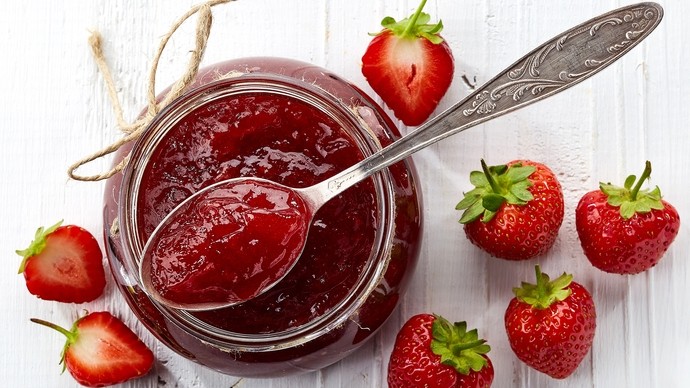 An spoon in an open jar of strawberry jam surrounded by fresh strawberries