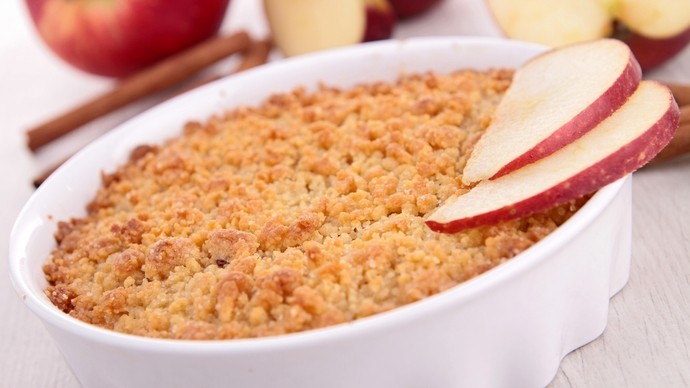 White dish of apple and bramble crumble with apple slices on side