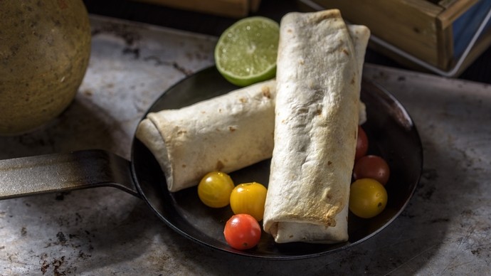 Two carefully wrapped burritos filled with haggis pictured on a plate with tomatoes