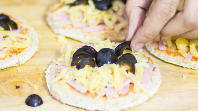 Preparation of a mini pizza topped with cheese, tomato sauce, ham and olives