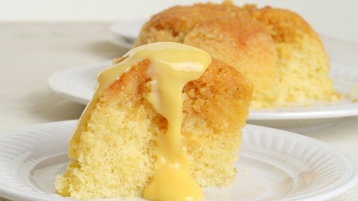 Two servings of golden soft sponge pudding on plates with custard