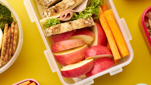 Three lunchboxes with different lunches inside - sandwiches, pasta, fruit and veg