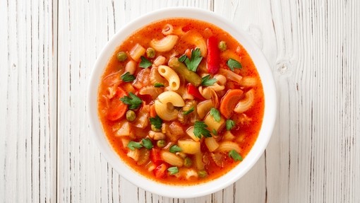 A vibrant bowl of orange minestrone soup containing an assortment of vegetables