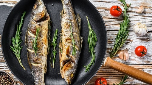 Two ses bass cooking in a frying pan with herbs