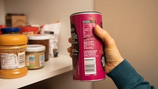 A hand holding a hot chocolate tub and putting it into a kitchen cupboard