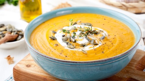 a vibrant creamy orange soup topped with pumpkin seeds