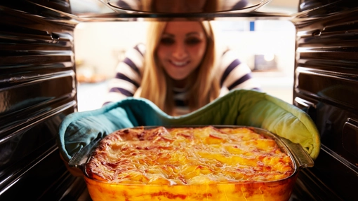 A person wearing oven gloves putting a dish in the oven.