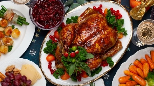 A birds eye view of a Christmas feast with a roast turkey in the centre, roasted root vegetables, a gravy boat and Christmas foliage spread around.