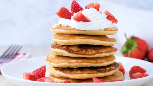 A stack of pancakes topped with strawberries and cream