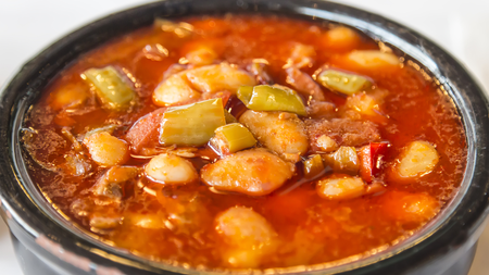 A vibrant pot of orange broth mixed with a variety of warming beans and veggies