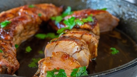 A sliced juicy pork fillet in a pan with leafy garnish