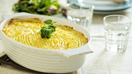 A golden shepherds pie in a white ceramic dish topped with a green garnish