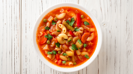 A vibrant bowl of orange minestrone soup containing an assortment of vegetables