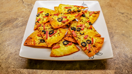 a plate full of crispy tortilla chips topped with tomato sauce and cheese