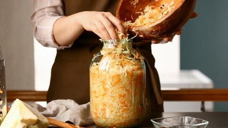 Hands pushing sauerkraut mix from a bowl into a large Kilner jar