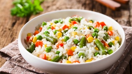 a large bowl of white rice mixed with bright veggies including garden peas and carrot