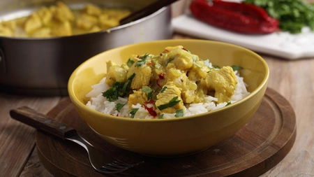 A bowl of turkey curry with rice on a table next to a larger serving bowl