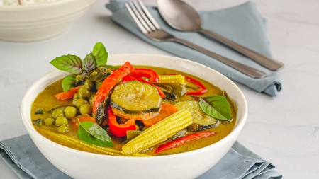 A bowl of Vegetable Thai curry on a table set with cutlery