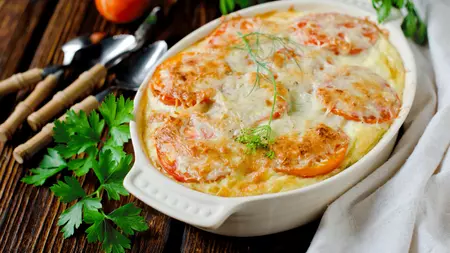 A traybake of golden turkey tomato gratin topped with whole tomato slices