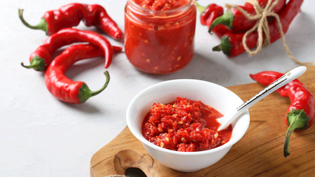 A bright red bowl of thick hot garlic and pepper sauce pictured next to chilli peppers