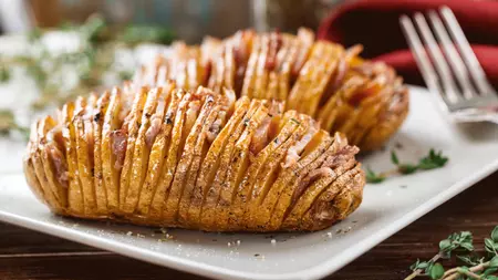 Sliced baked golden Hasselback potato topped with lardons