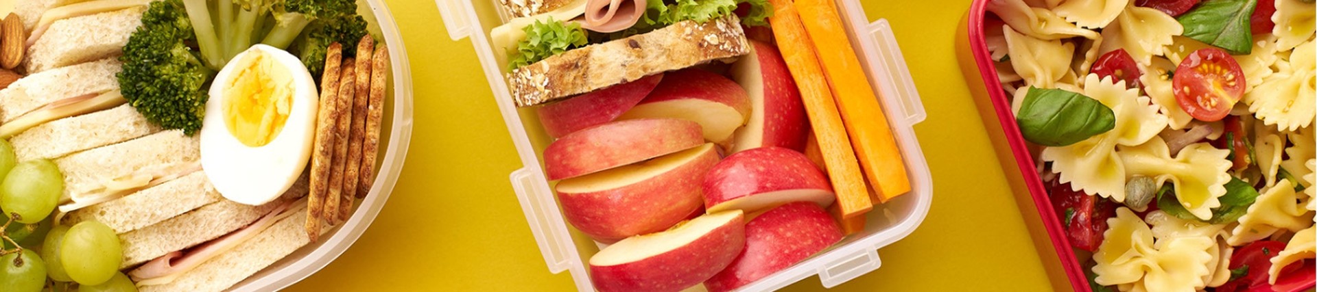 Three lunchboxes with different lunches inside - sandwiches, pasta, fruit and veg