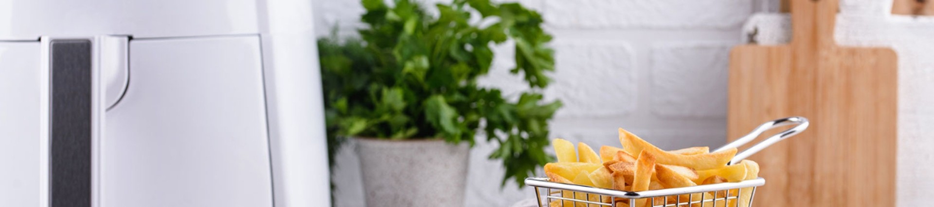 An air-fryer showing a small basket full of chips, with leafy herbs dotted around the image.