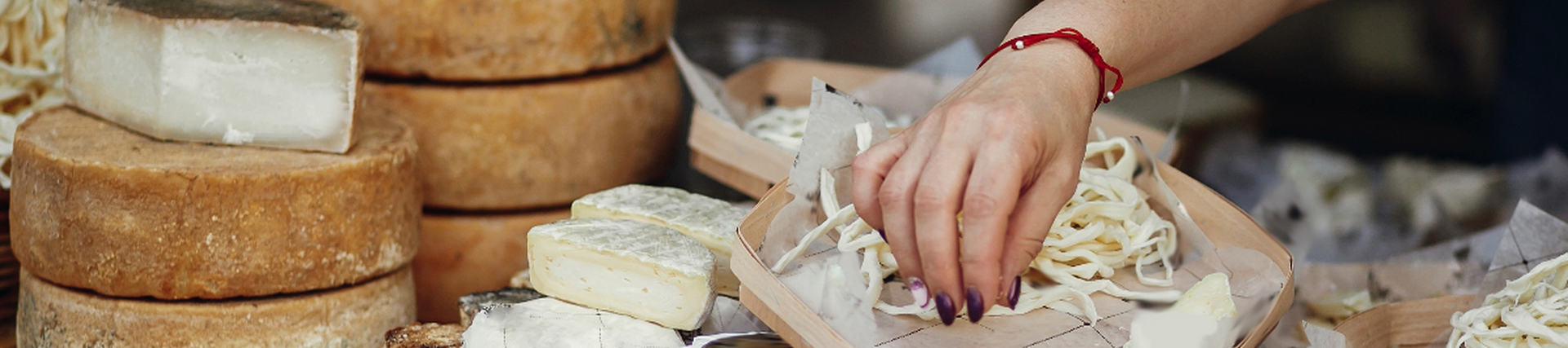A stall table with many different cheeses in different wax. A white hand is grabbing grated cheese from the table